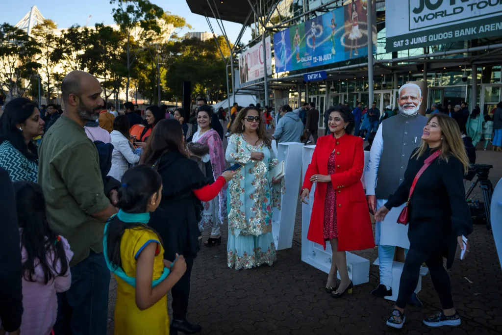 Visitors lining up to take photos with a cardboard cut out of Mr. Modi during a rally in Sydney. Groups had reached the event by bus and flights chartered by a local B.J.P. chapter.Credit...Matthew Abbott for The New York Times