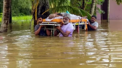 People wade through a flooded area as they carry a sick elderly man to a hospital, in Thiruvalla.(PTI)