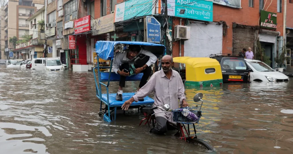 A man rides his cycle rickshaw with a passenger through a flooded street after heavy rains in New Delhi. [Anushree Fadnavis/Reuters]  9 Jul 2023