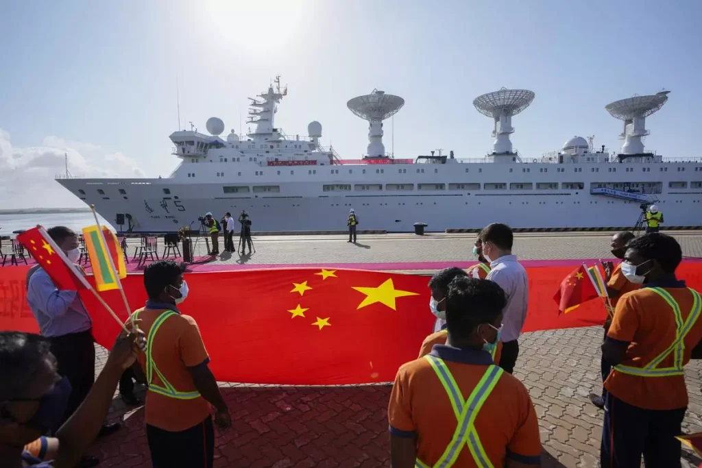 Sri Lankan workers hold the Chinese flag to welcome the Chinese research ship Yuan Wang 5 as it arrives at Hambantota International Port in Sri Lanka in August 2022. China’s Belt and Road initiative has built power plants, roads, railroads, and ports around the world and deepened its relations with Africa, Asia, Latin America, and West Asia. | Photo Credit: Eranga Jayawardena/AP